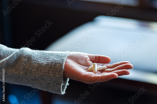 Closeup image of a woman holding white medicine capsules in hand