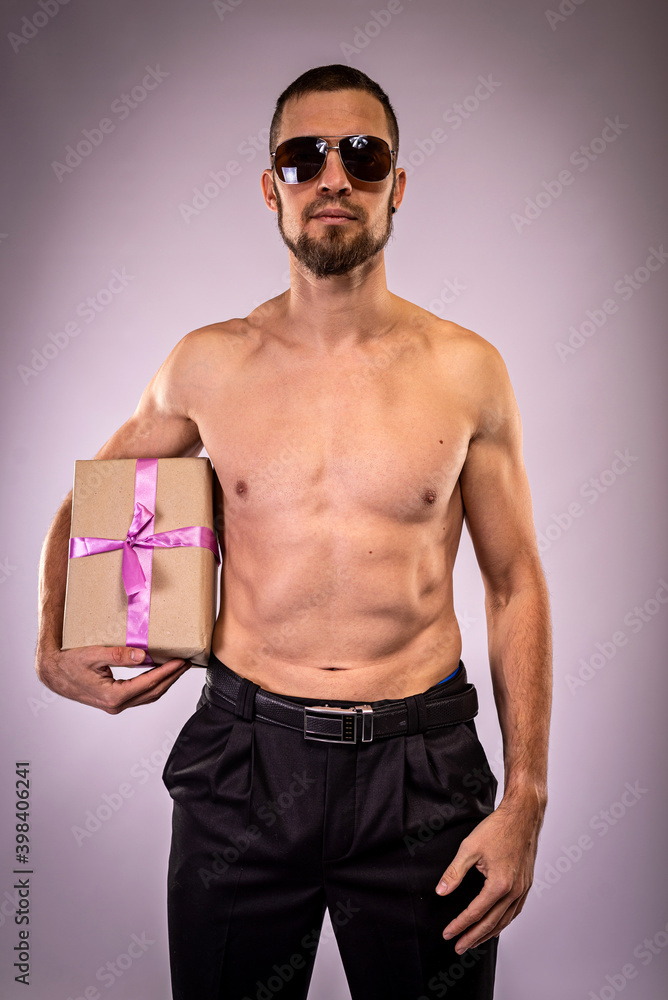 A sporty man in sunglasses with a naked torso holds a gift close-up.