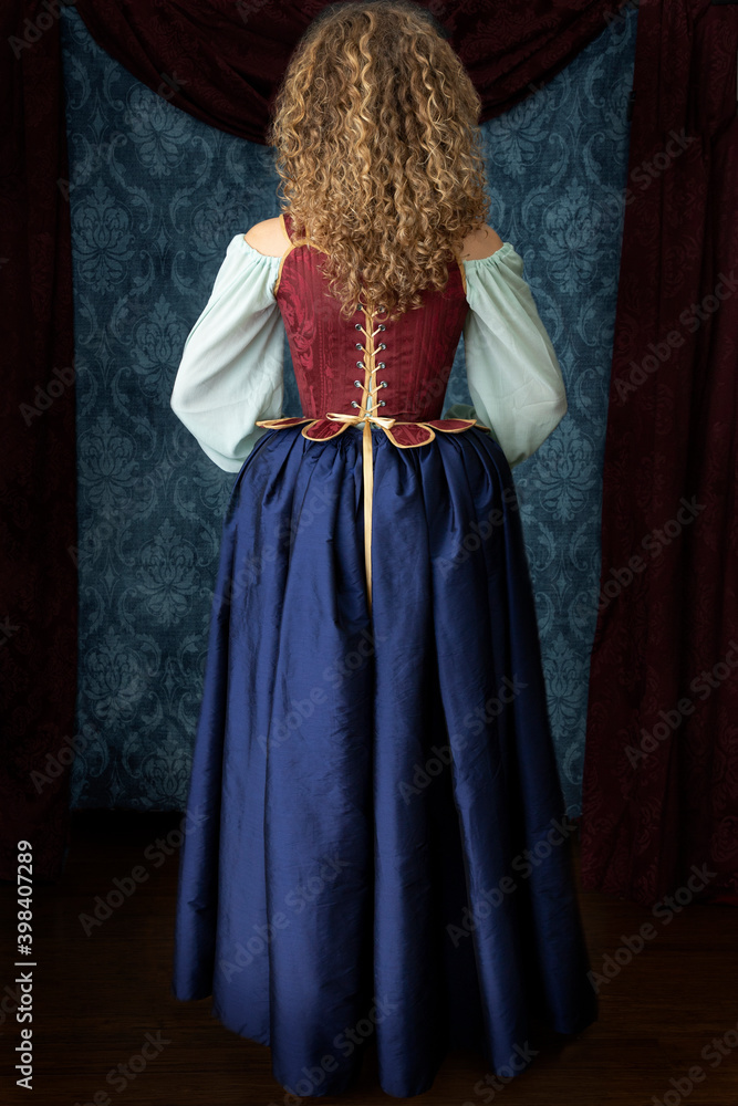 A young renaissance woman wearing a red corset and blue silk skirt