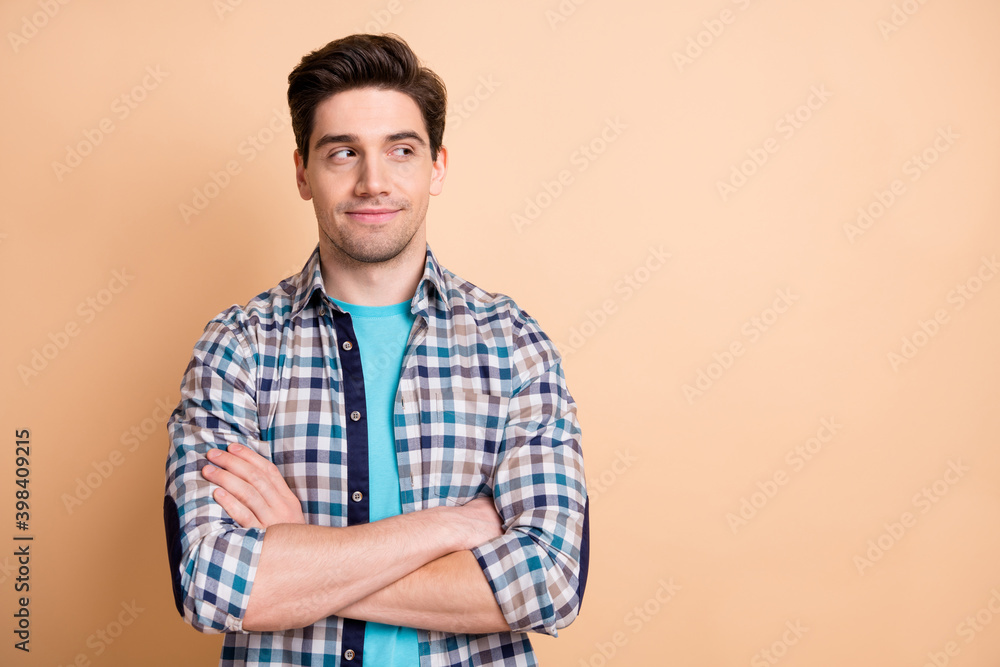 Portrait of nice cheery guy wear checked shirt folded arms looking copy empty place space isolated over beige pastel color background Portrait of nice cheery guy wear checked shirt folded arms looking copy empty place space isolated over beige pastel color background