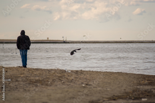 Sylwetka mężczyzny stojącego na brzegiem wody z przelatującym obok ptakiem