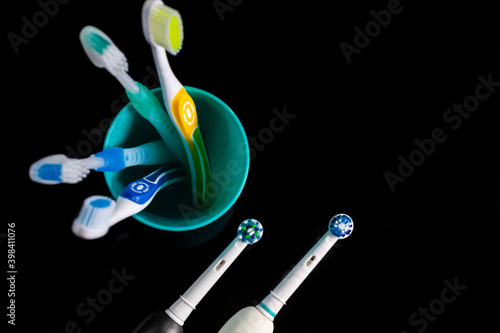 Professional Electric Toothbrushes In Front of Four Manual Toothbrushes Placed on One Cup Together On Black. Horizontal Image