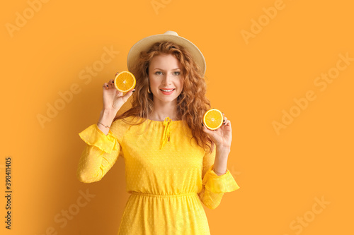 Beautiful young woman with cut orange on color background