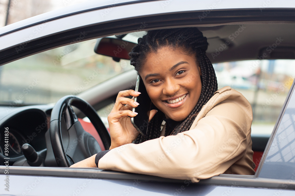Happy girl driving a car with a phone, African-American