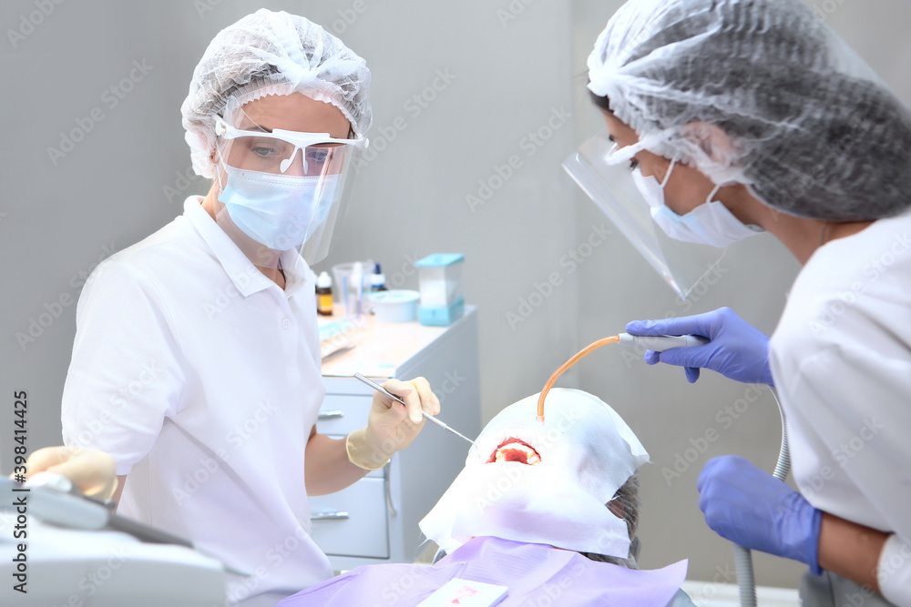 The dentist and assistant perform professional dental cleaning for the patient. Protective screen and medical mask on the face. The concept of health. The dentist and assistant perform professional dental cleaning for the patient. Protective screen and medical mask on the face. The concept of health.