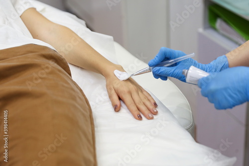 the hands of a beautician doctor apply anesthetic cream to the patient's hands