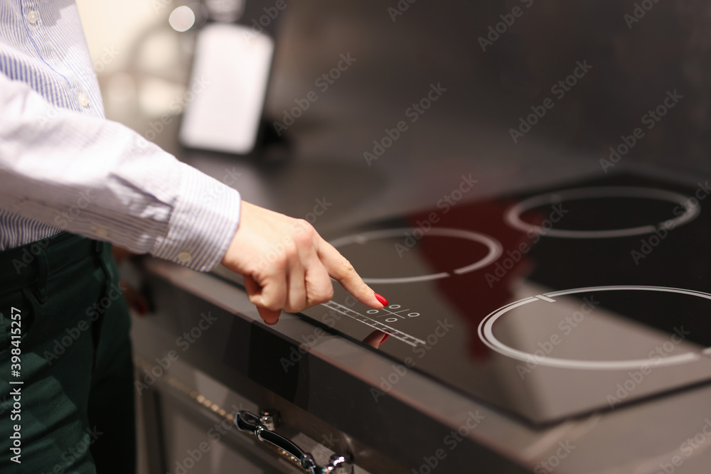 Female finger presses button on touch electric stove