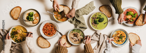 People eating Autumn and Winter creamy vegan soups  fall and winter vegetarian food menu. Flat-lay of peoples hands eating homemade soup with fresh bread over white table background  top view