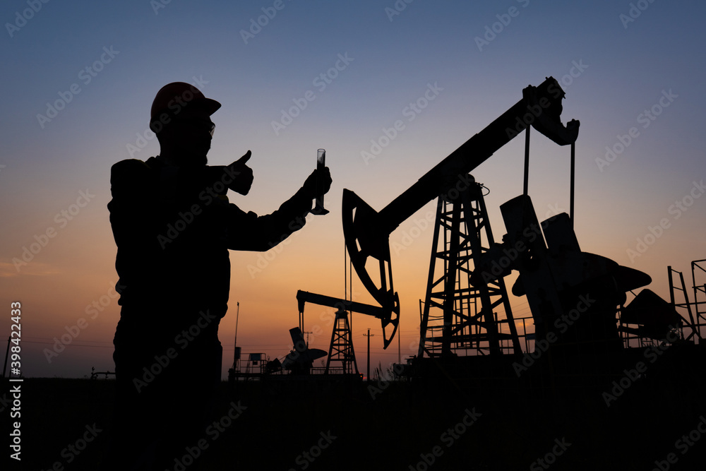 Silhouette of a chemical engineer taking a sample of crude oil against the background of oil pumps.