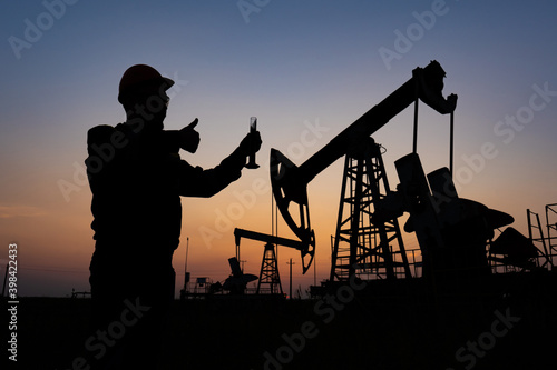 Silhouette of a chemical engineer taking a sample of crude oil against the background of oil pumps.