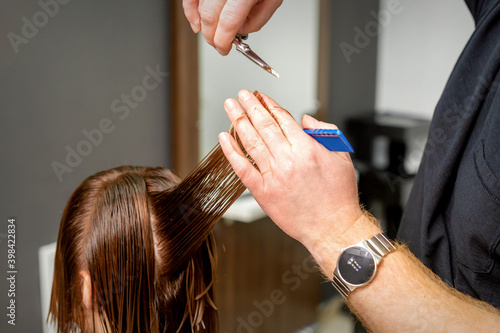 Close up of male hairdresser's hands cuts female hair in a hair salon