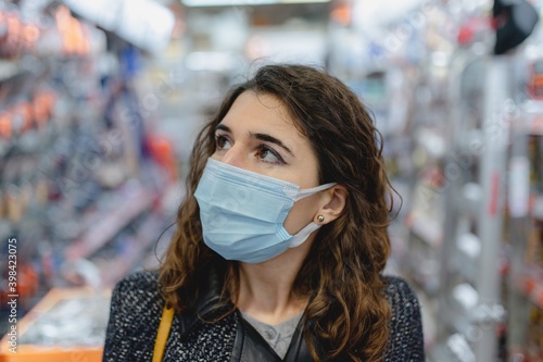 Close-up caucasian young woman wearing protective face mask doing shopping in store.