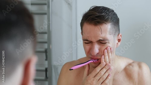 Young man brushing his teeth in bathroom and stop becuse of a tooth pain photo