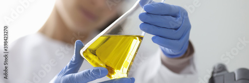 Female hands in rubber gloves holding flask with urine analysis in clinical laboratory closeup. Research on quality of oil products concept.