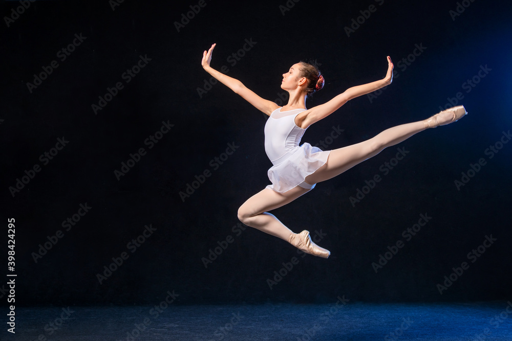 Ballerina in a white dress flying in a jump on black background