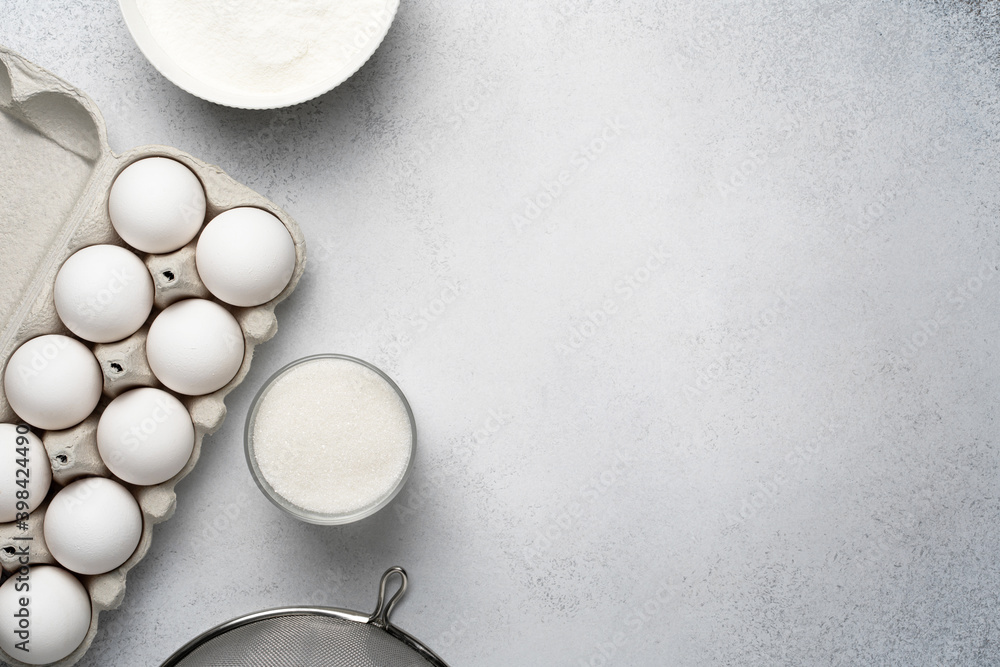 Wheat flour, sugar, sieve and white eggs on the grey background. Baking ingredients for cake. Top view, copy space. Wheat flour, sugar, sieve and white eggs on the grey background. Baking ingredients for cake. Top view, copy space.