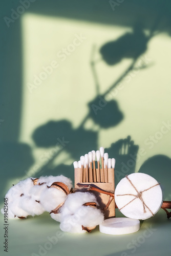 eco-friendly biodegradable plastic free ear swabs and cotton pads on the green background with cotton flowers photo