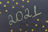 Christmas and New Year concept. Chalk handwritten inscription 2021 on a black board. With golden stars. 