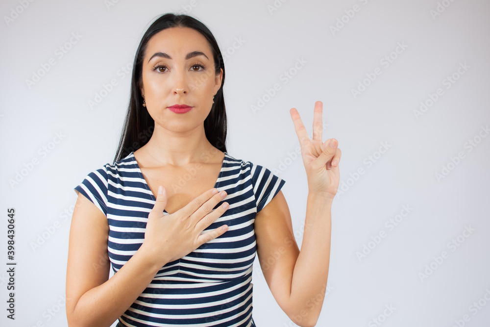 Portrait of gorgeous brunette woman in striped t-shirt looking at camera with smile and showing peace sign with fingers isolated over white background Portrait of gorgeous brunette woman in striped t-shirt looking at camera with smile and showing peace sign with fingers isolated over white background
