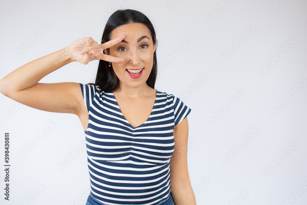 Portrait of gorgeous brunette woman in striped t-shirt looking at camera with smile and showing peace sign with fingers isolated over white background Portrait of gorgeous brunette woman in striped t-shirt looking at camera with smile and showing peace sign with fingers isolated over white background
