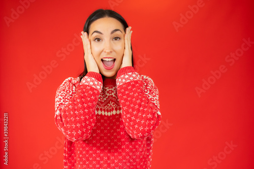 Young woman in winter sweater surprised over red background.
