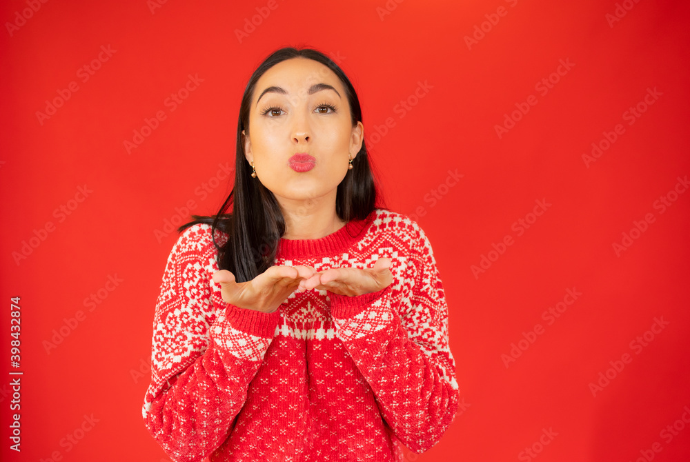 Young woman in winter sweater sending a kiss over red background. Young woman in winter sweater sending a kiss over red background.