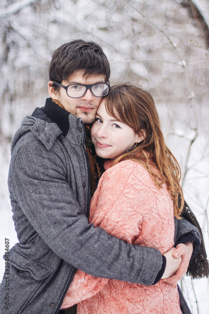 Fototapeta premium A couple - a man with glasses and a young girl in winter clothes hugging in a winter forest