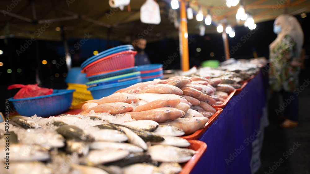 Street food night market at  Putrajaya, near Kuala Lumpur. A seafood stand, the fish are lying on the counter. In the background a customer is waiting