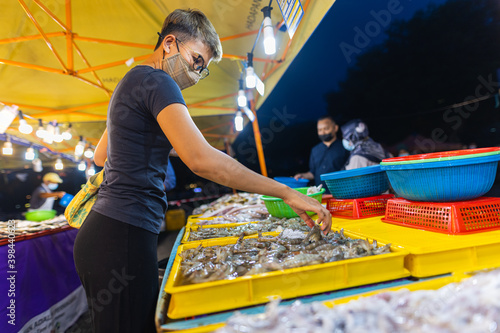 Street food night market at Putrajaya, near Kuala Lumpur. Young asian girl buys seafood in a night market. Malaysian women with face mask in a street market