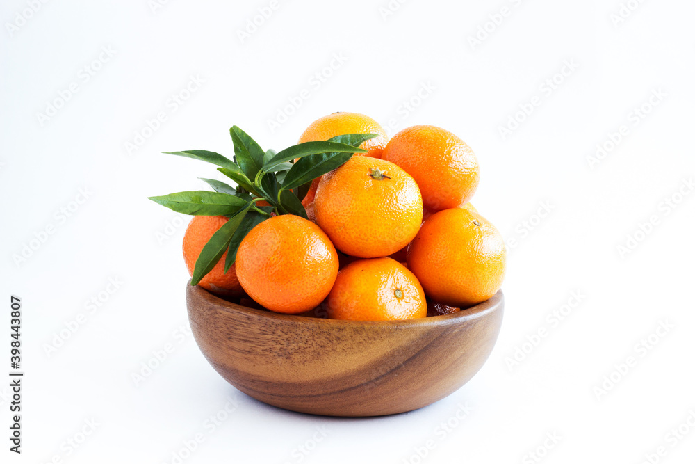 Tangerines or clementines with green leaf in a wooden bowl isolated on white background. A traditional treat for Christmas and New Years. Farm products. Healthy eating. Consumption of fresh fruits. Tangerines or clementines with green leaf in a wooden bowl isolated on white background. A traditional treat for Christmas and New Years. Farm products. Healthy eating. Consumption of fresh fruits.