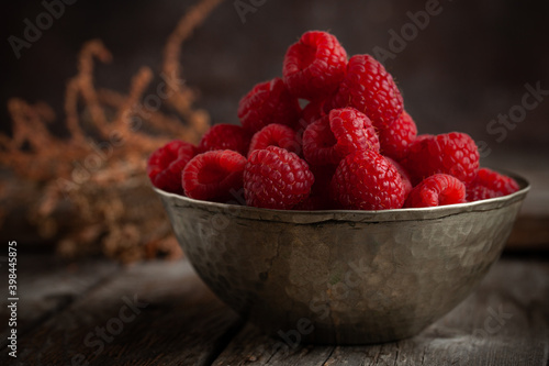 Fresh raspberries in vintage copper bowl on natural wooden background.