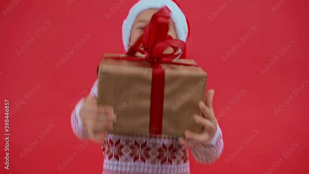 happy girl in santa hat and christmas sweater jumping with gift isolated on red happy girl in santa hat and christmas sweater jumping with gift isolated on red