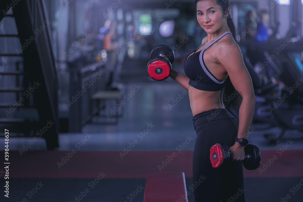 Young woman with sweat doing exercises, working out with dumbbell in fitness gym. Strong and healthy concept. Selected focus.