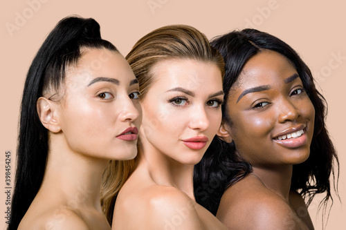 Close up beauty collage portrait of three young multiracial female models with naked shoulders and beautiful pure skin, looking on camera, on light beige studio background. World beauty