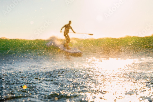 Stand Up Paddle surfing on wave and water drops with bokeh.