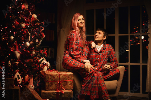 a man and a woman in red pajamas are sitting at night near the christmas tree