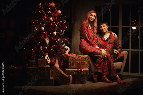 a man and a woman in red pajamas are sitting at night near the christmas tree