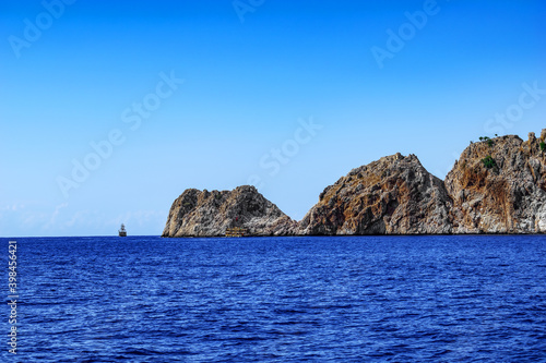 Rocky coast of the peninsula in Alanya against the background of the sea horizon with two tourist ships (Turkey). Seascape with bare stone mountains in the middle of blue water