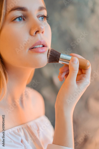 The girl does makeup. Applies powder to the face with a kabuki brush.