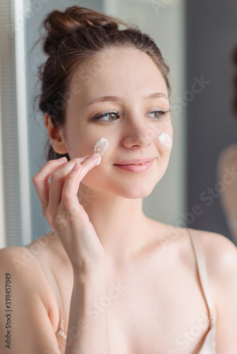 The girl applies cream to her face. Skin care at home in the bathroom.