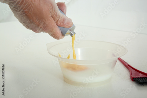 Woman preparing dye for hair coloring at white table, closeup