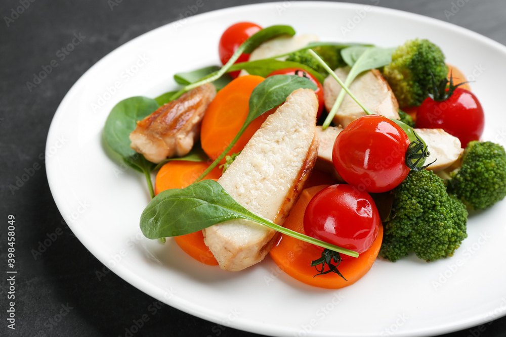 Delicious salad with chicken, vegetables and spinach on black table, closeup Delicious salad with chicken, vegetables and spinach on black table, closeup
