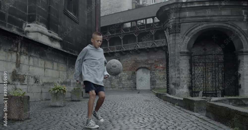 Capable teenager guy kicking football ball with feet . Young talanted boy s practicing tricks at old european city street. Concept of sport, talent and lifestyle Capable teenager guy kicking football ball with feet . Young talanted boy s practicing tricks at old european city street. Concept of sport, talent and lifestyle