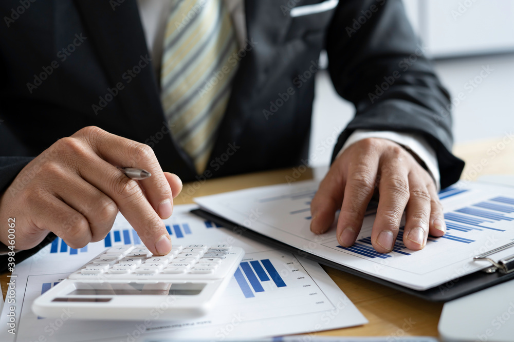 Close-up of businessmen or accountants holding a pen and pressing on the calculator to calculate business information, Finance documents, business ideas. Close-up of businessmen or accountants holding a pen and pressing on the calculator to calculate business information, Finance documents, business ideas.