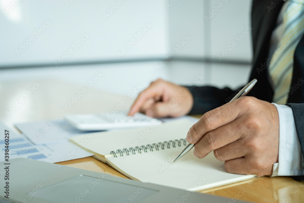 Close-up of businessmen or accountants holding a pen and pressing on the calculator to calculate business information, Finance documents, business ideas. Close-up of businessmen or accountants holding a pen and pressing on the calculator to calculate business information, Finance documents, business ideas.