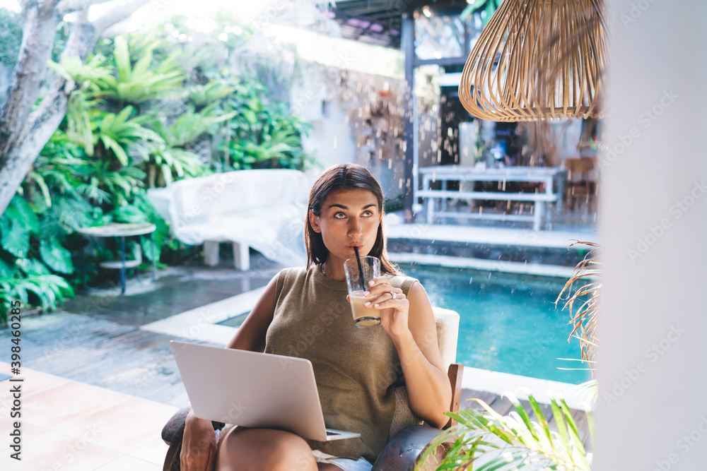 Delighted lady drinking beverage from straw and surfing laptop