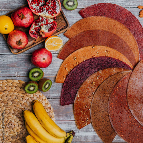 Many colorful fruit leathers with fresh fruits on the wooden table. Round fruit leather. Healthy food. Apples, bananas, nuts, lime, kiwifruits, pomegranate top view.
