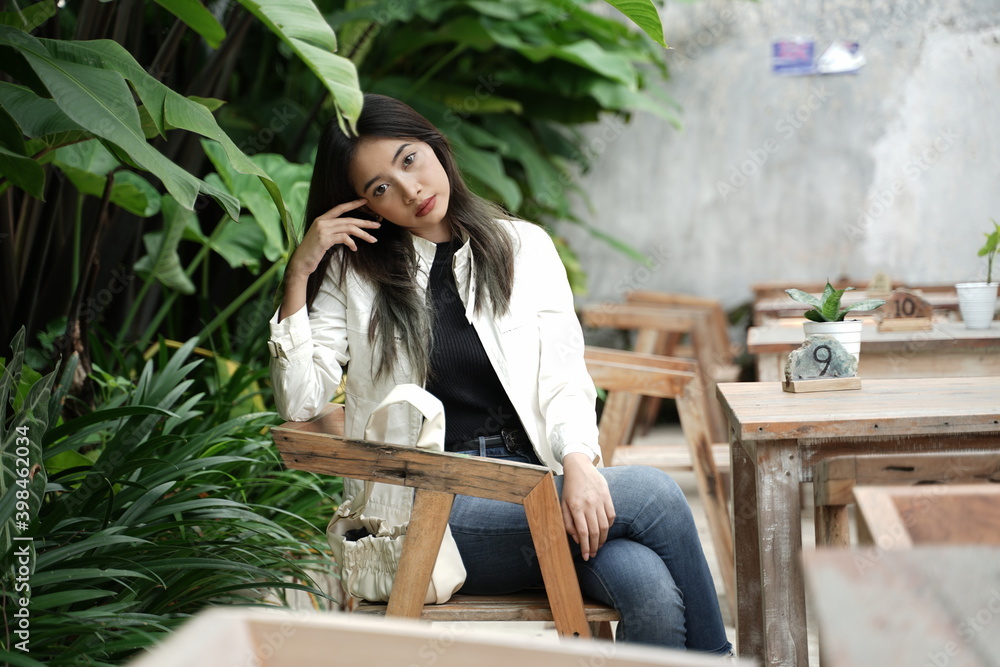 Beautiful girl is sitting pretty on a wooden chair in a cafe, in the afternoon waiting for dusk. Natural light shining on add to the beauty of the model. Young women are waiting in the garden. Beautiful girl is sitting pretty on a wooden chair in a cafe, in the afternoon waiting for dusk. Natural light shining on add to the beauty of the model. Young women are waiting in the garden.