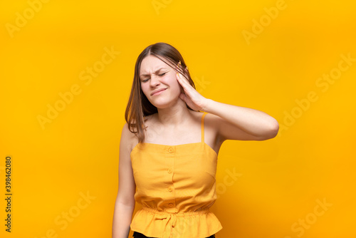 Beautiful Caucasian woman in a yellow sweater holds her ear on a yellow background. Ear treatment. Emphasized by a girl suffering from noise.