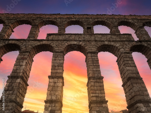 Bello atardecer en tonos anaranjados y azules, visto a través de los arcos del acueducto romano de Segovia, en Castilla y León,España